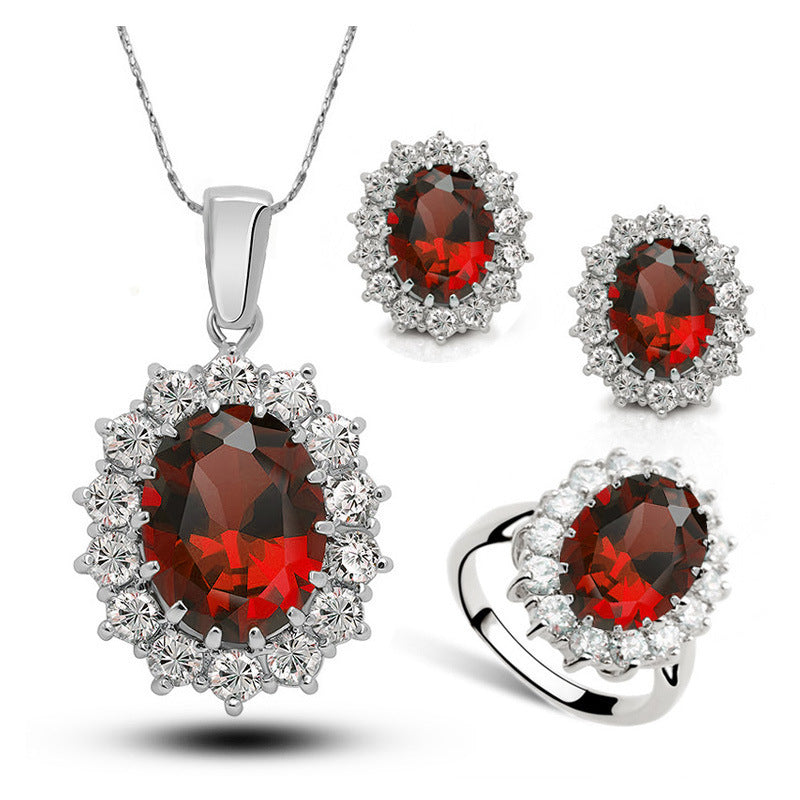 Crystal bridal jewelry set with red round halo gemstones on necklace, earrings, and ring, silver.