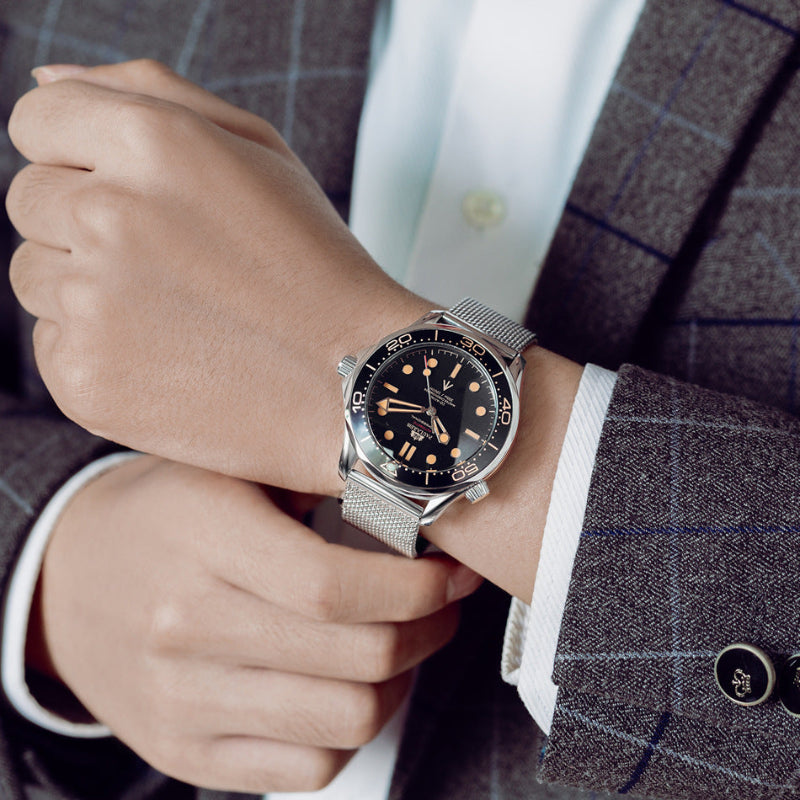 Person wearing a silver watch with a black face on a suit sleeve.