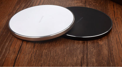 Two wireless charging pads, one white and one black, on a wooden surface.