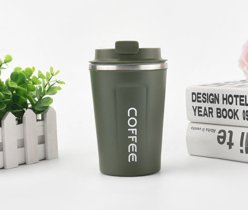 Green coffee tumbler with 'COFFEE' text on a white surface with a plant and books in the background.