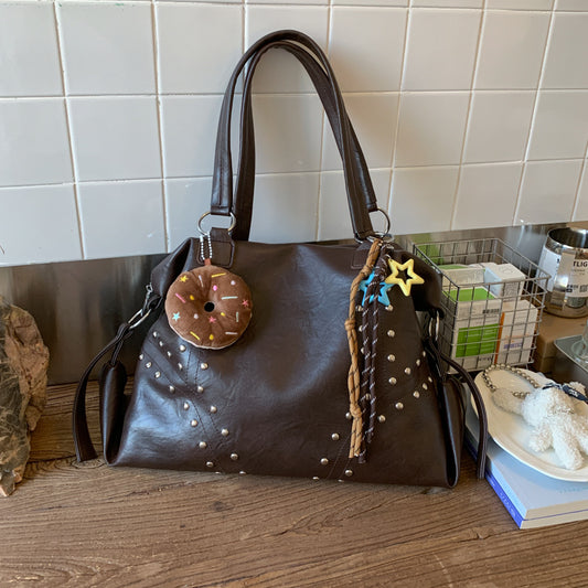 Brown handbag with decorative elements on a wooden surface with a tiled wall background