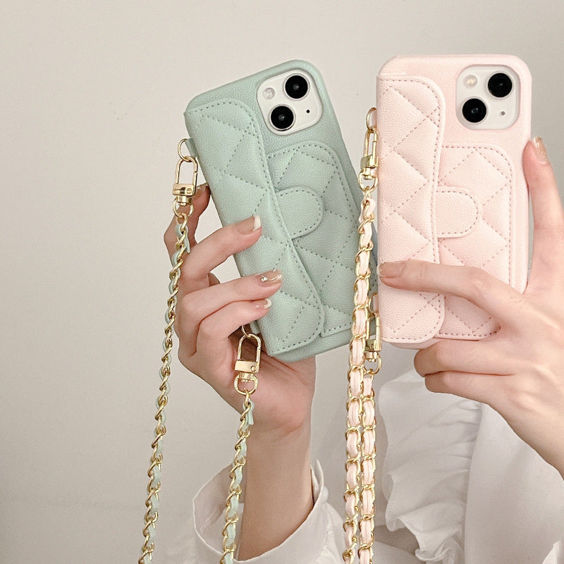 Two phone cases, one green and one pink, held by hands with a gold chain strap.