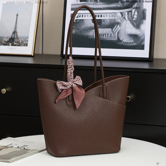 Brown tote bag with a bow on a surface with framed pictures in the background