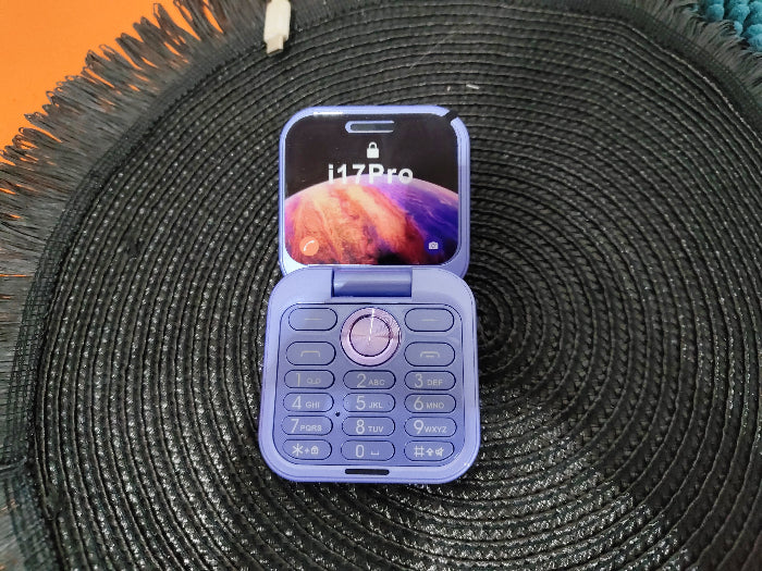 Lavender folding flip phone with open keypad and front display on a textured mat