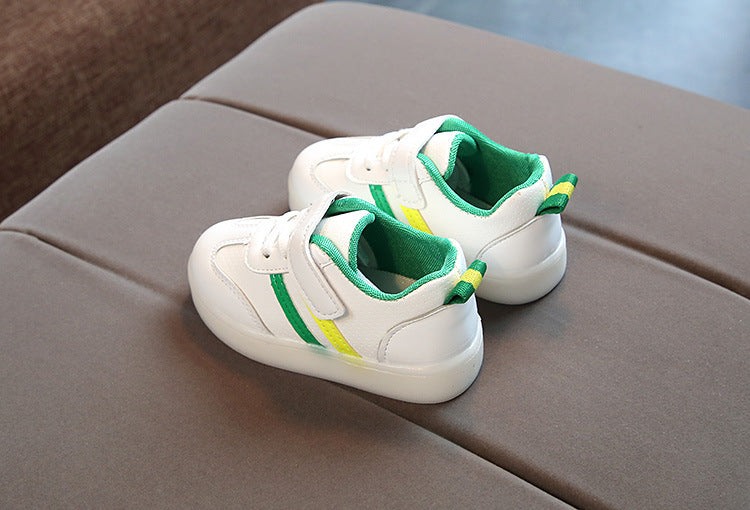 Kids white LED light-up sneakers with green accents; pair resting on couch