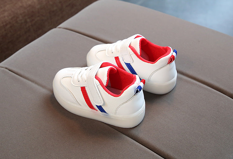 Kids white LED light-up sneakers with red and blue stripes; back view on couch