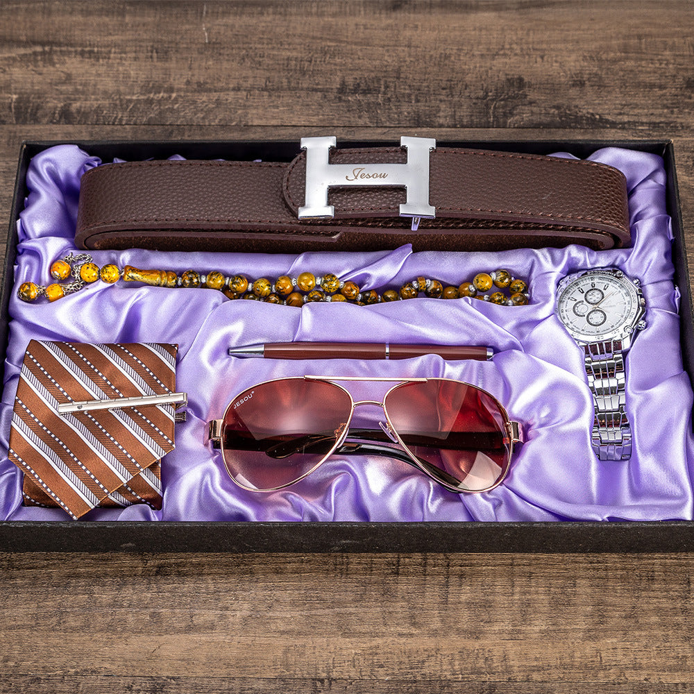 Men's gift set six-piece laid flat: brown belt, sunglasses, watch, beaded necklace, tie.