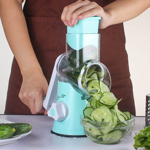 Teal manual rotary slicer producing cucumber slices, with hand holding top container
