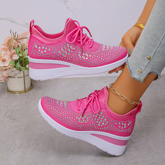 Pink sneakers with rhinestone details worn by a person on a light gray background