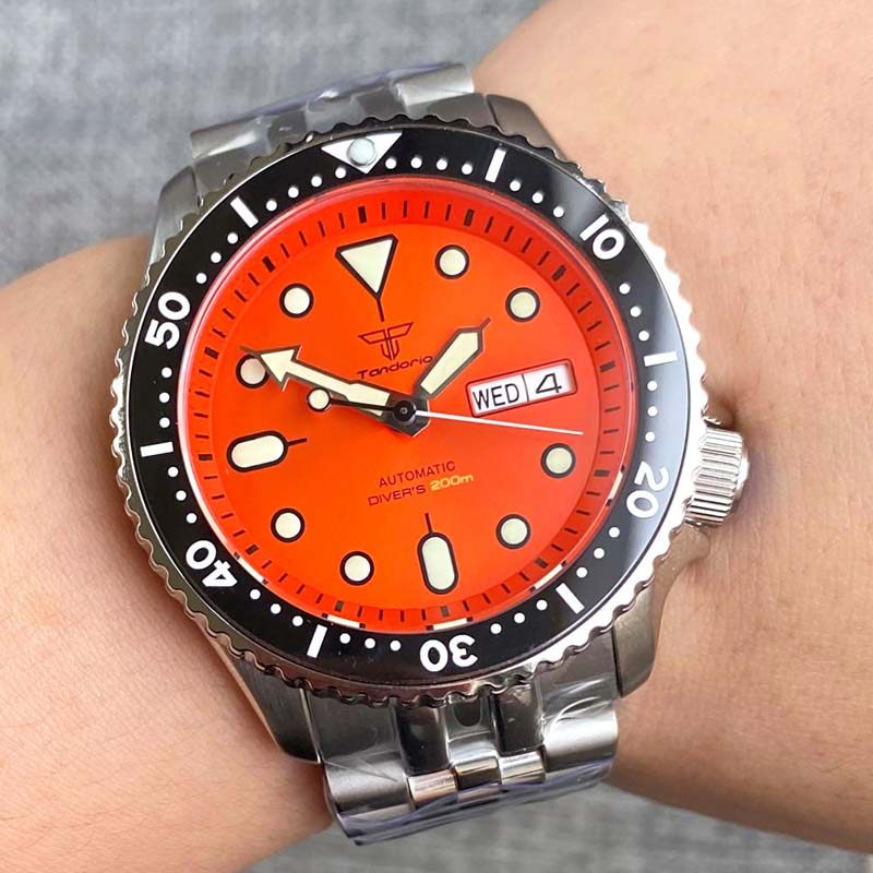 Watch with an orange face and silver case on a wrist against a gray background