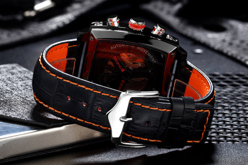Luxury watch with black strap and orange stitching on a textured surface