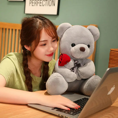 Woman using a laptop with a large teddy bear holding a rose on her lap. YAXSO UAE ONLINE STORE