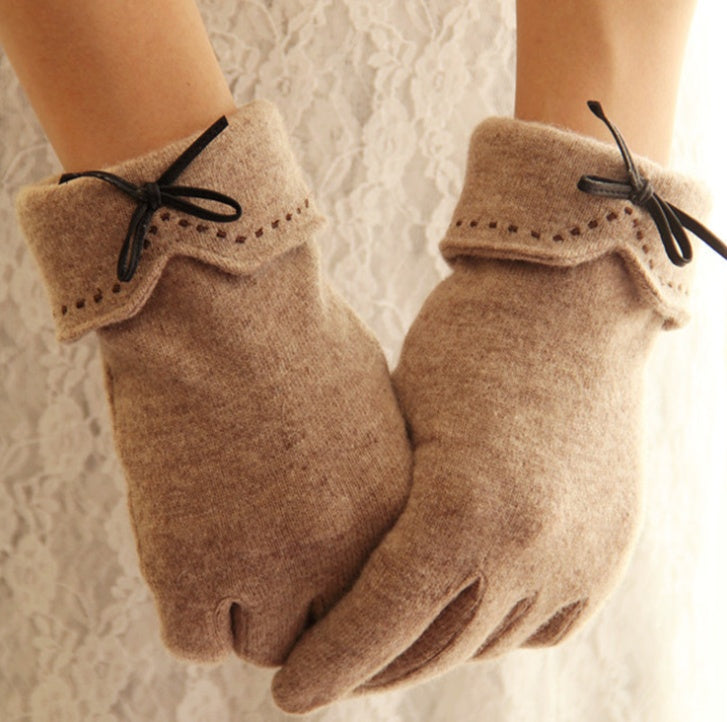 Pair of beige gloves with black ribbons on a textured white background