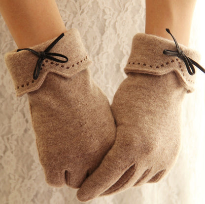 Pair of beige gloves with black ribbons on a textured white background