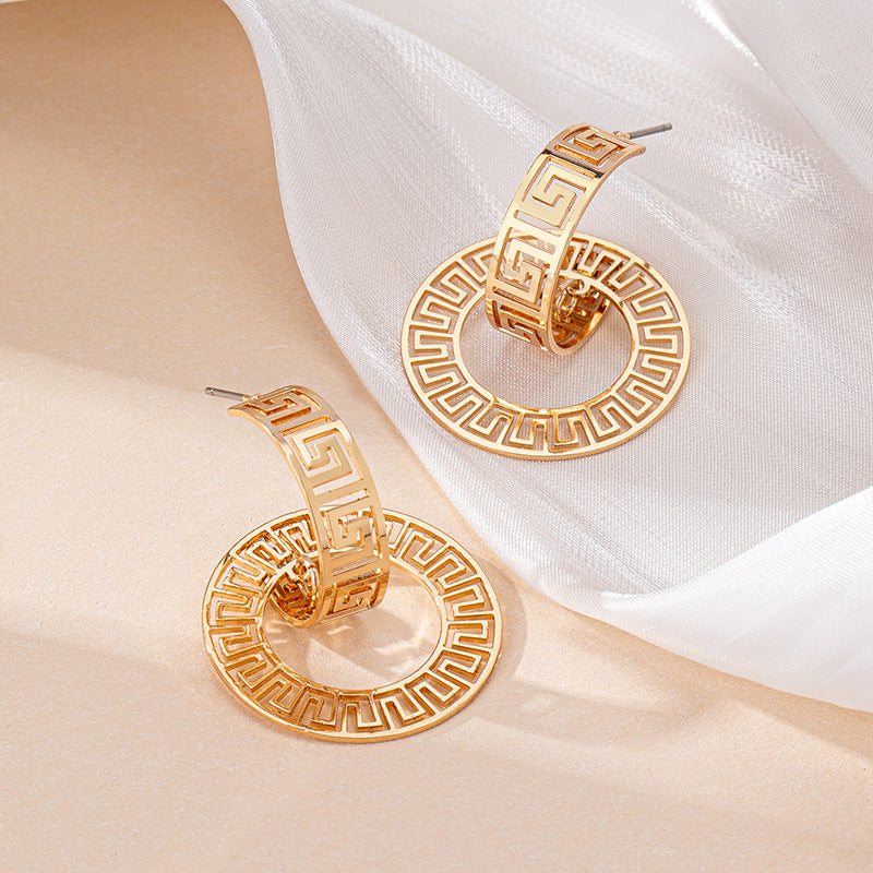 Gold-tone geometric hoop earrings with Greek key pattern, close-up