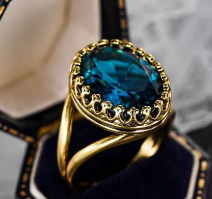 Teal-blue oval gemstone ring with gold ornate bezel and court-style curved band