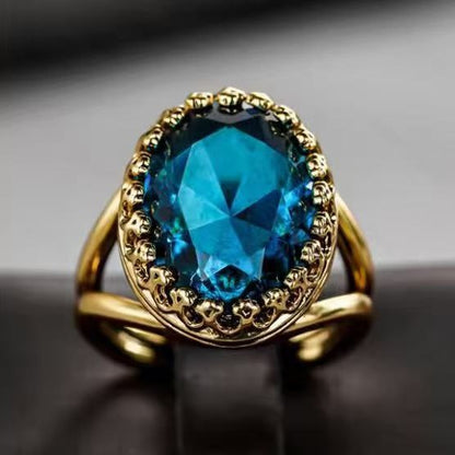 Front view gold ring with oval teal-blue faceted stone and engraved decorative bezel