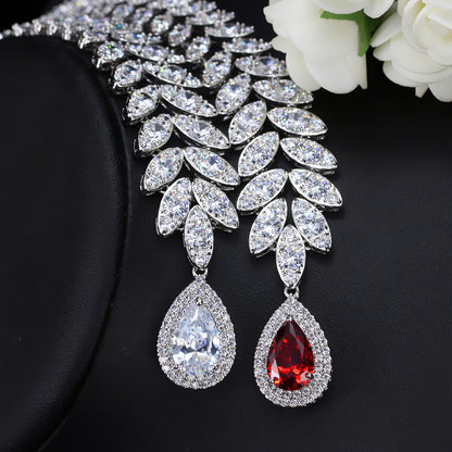 Pair of teardrop-shaped earrings with clear and red gemstones on a black background.