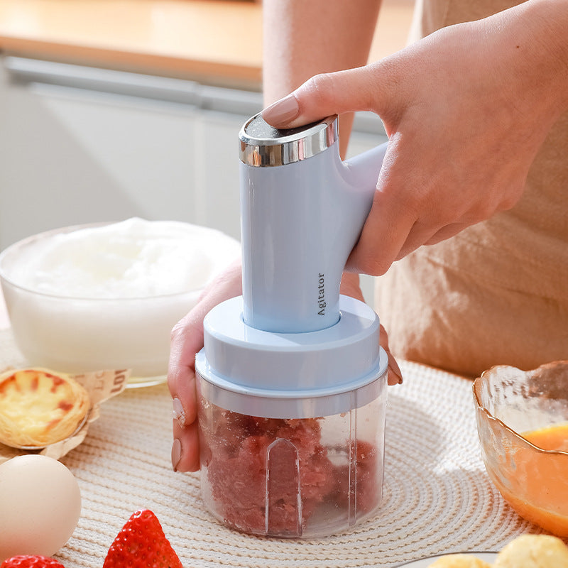 Electric whisk hand blender in white, held over a clear mixing cup with attached wire whisk beaters