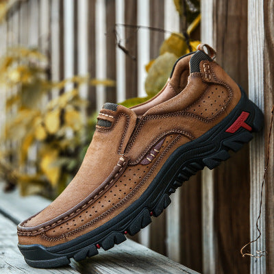 Brown leather shoe with black sole on a wooden surface with blurred plants in the background