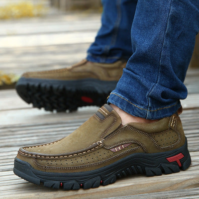 Brown leather shoes worn with blue jeans on a wooden floor.