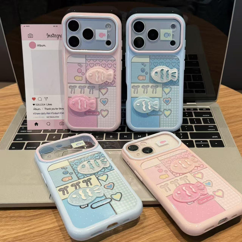 Two iPhone cases on a desk: pale blue and pink with hearts and raised 3D fish
