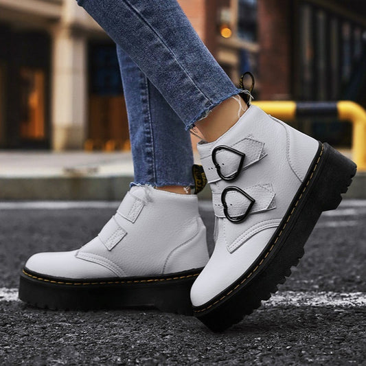 White boots with black soles worn by a person on a street.