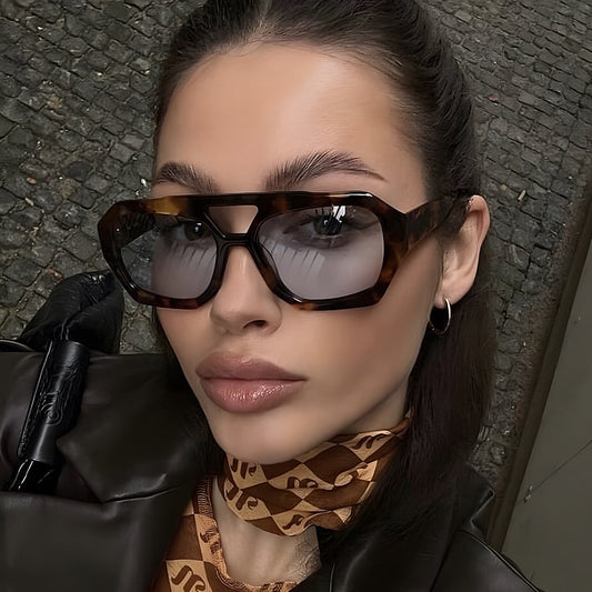 Woman wearing sunglasses and a patterned scarf with a textured wall background