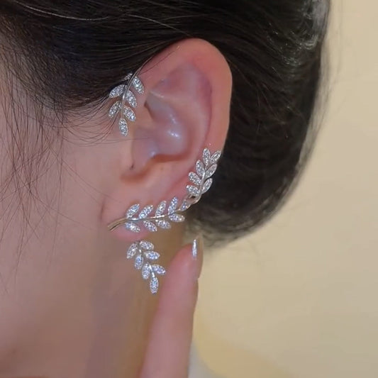 Close-up of an ear wearing a silver leaf-shaped earring with a blurred background