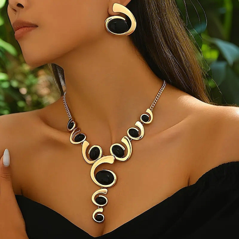 Woman wearing a gold and black necklace with matching earrings against a blurred green background