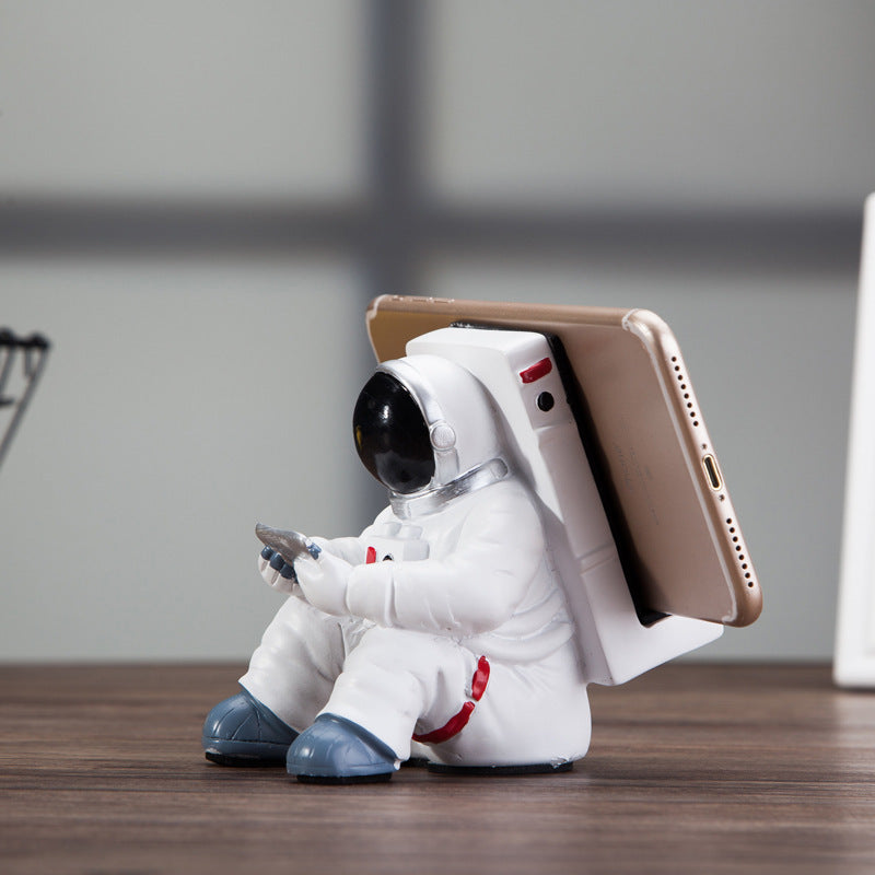 Astronaut mobile phone stand holding a phone upright, white suit with blue boots