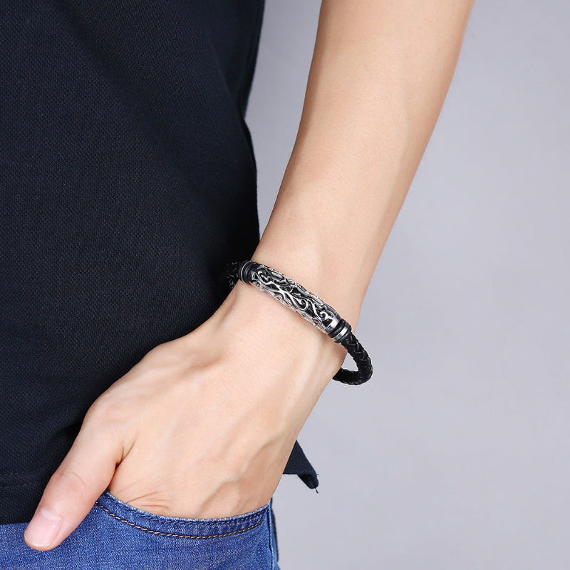 Person wearing a black braided bracelet with intricate design on a plain background