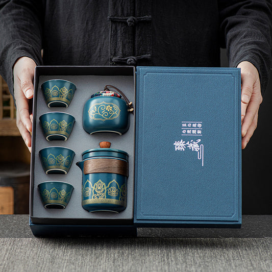 Set of blue ceramic tea cups and teapot in a gift box held by a person.
