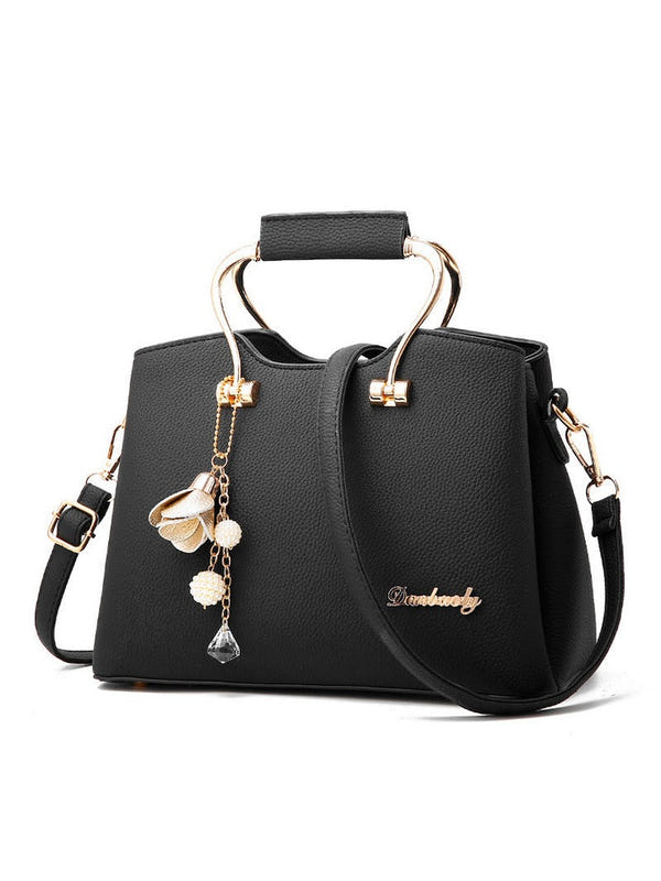 Black handbag with structured top handle, crossbody strap, gold-tone clasps, and charm tassel