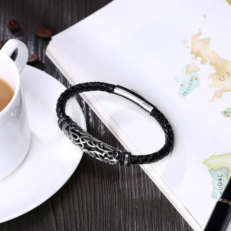 Black braided leather bracelet with silver clasp on a wooden surface with a cup of coffee and map.
