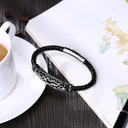 Black braided leather bracelet with silver clasp on a wooden surface with a cup of coffee and map.