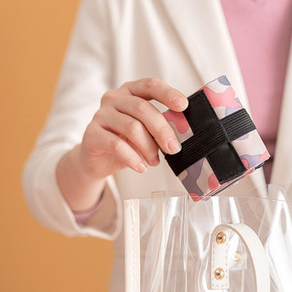 Hand holding a small, colorful pouch with a black strap against a blurred background