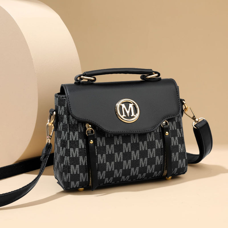 Black monogram crossbody handbag with flap top, gold M emblem, leather shoulder strap