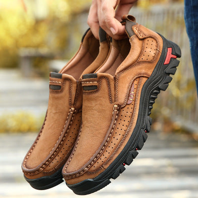 Brown leather shoes with black soles held by a hand against a blurred outdoor background