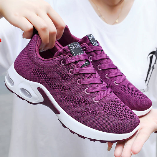 Purple running shoes with white soles held by a person against a white background