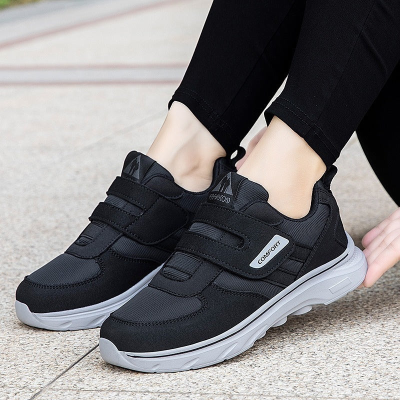 Black lightweight casual sneakers on feet with hook-and-loop straps and white sole