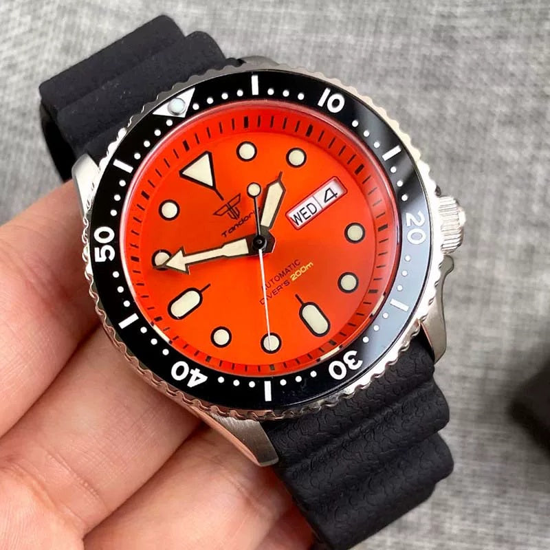 Wristwatch with a red face and black strap held in a hand against a gray background