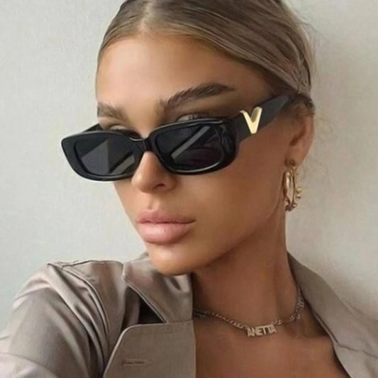 Person wearing black sunglasses with gold accents against a plain background