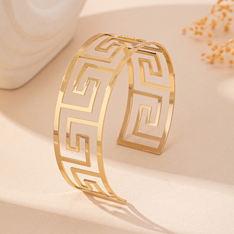 Gold-tone geometric Greek key cuff bracelet, close-up of engraved pattern