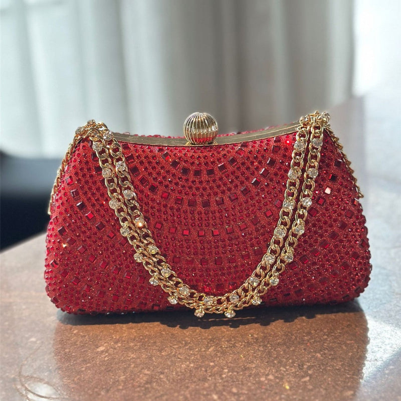 Red handbag with gold chain handle on a reflective surface