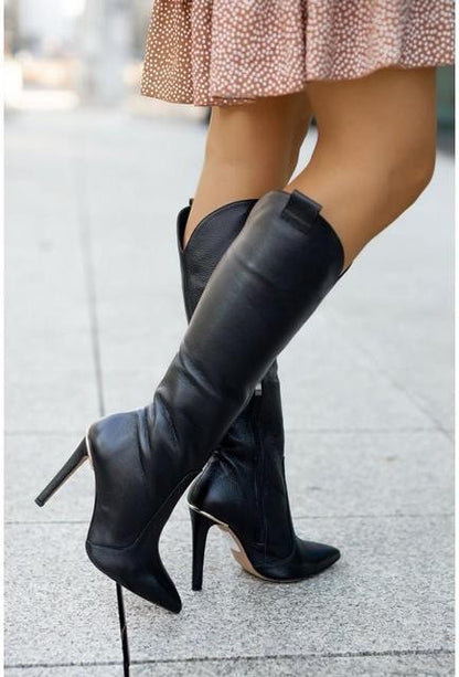 Black knee-high boots with high heels worn by a person on a sidewalk.