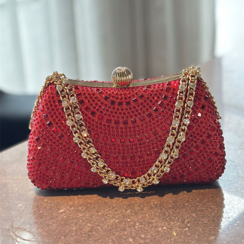 Red handbag with gold chain strap on a reflective surface