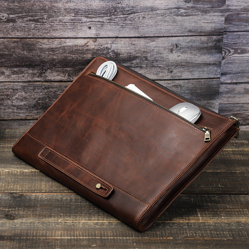 Brown leather laptop bag with front pocket and zipper closure, metal logo tab