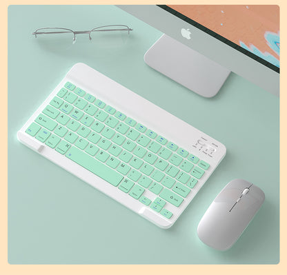 Keyboard with mint green keys on a desk with a computer and glasses.