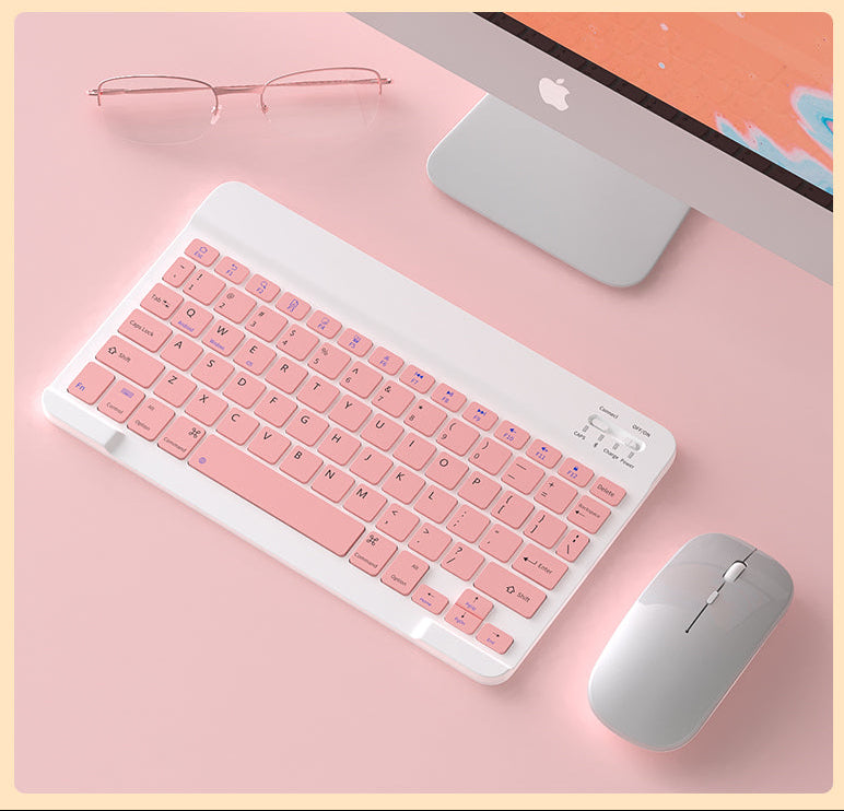 Pink keyboard and mouse set on a pink surface with an Apple computer in the background.